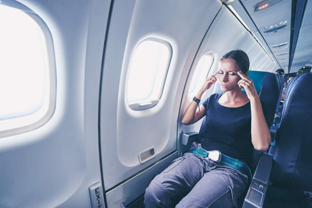 Kvinde i flysæde med lukkede øjne og fingrene på sine tindinger.